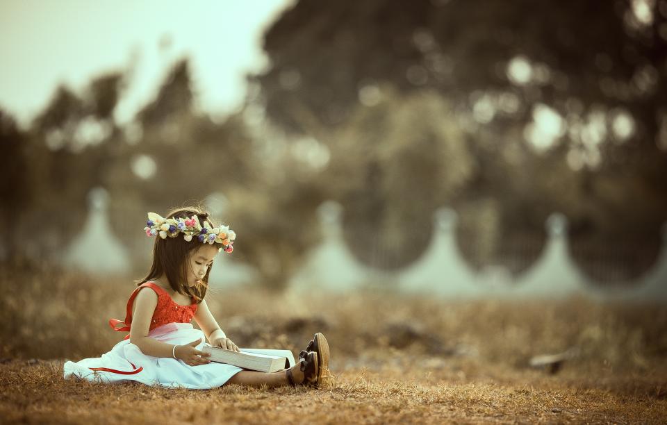 Une enfant plongée dans son livre personnalisé, installée dans l’herbe