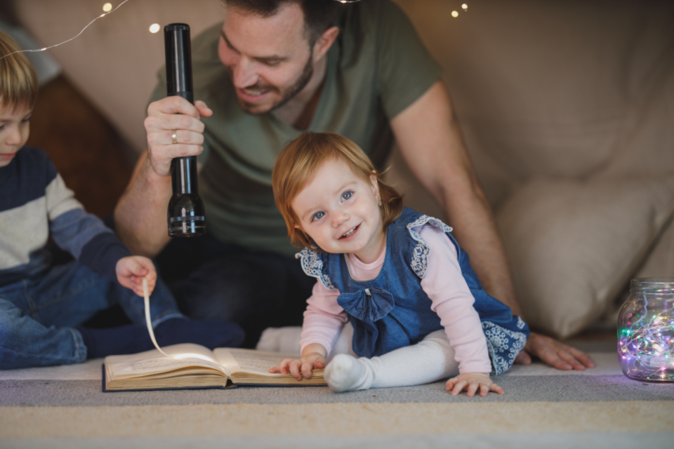 Une famille lit une histoire à la lampe torche, blottie sous un tipi de couvertures