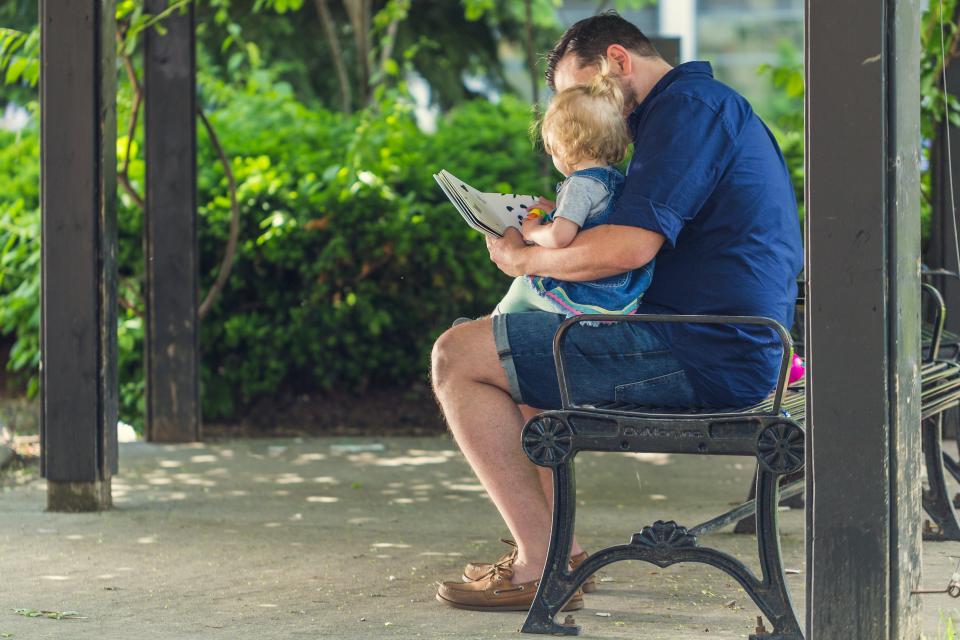 Un père lit une histoire personnalisée avec sa fille, assis sur un banc